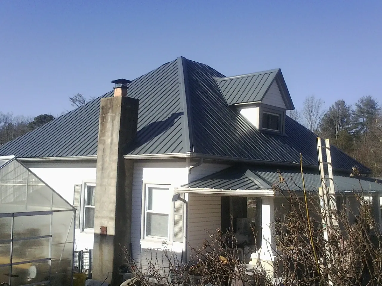 Dark blue standing seam metal roof on a white farmhouse with dormer — Slate & Tile Roof Repair by Roofing Brothers in Epsom
