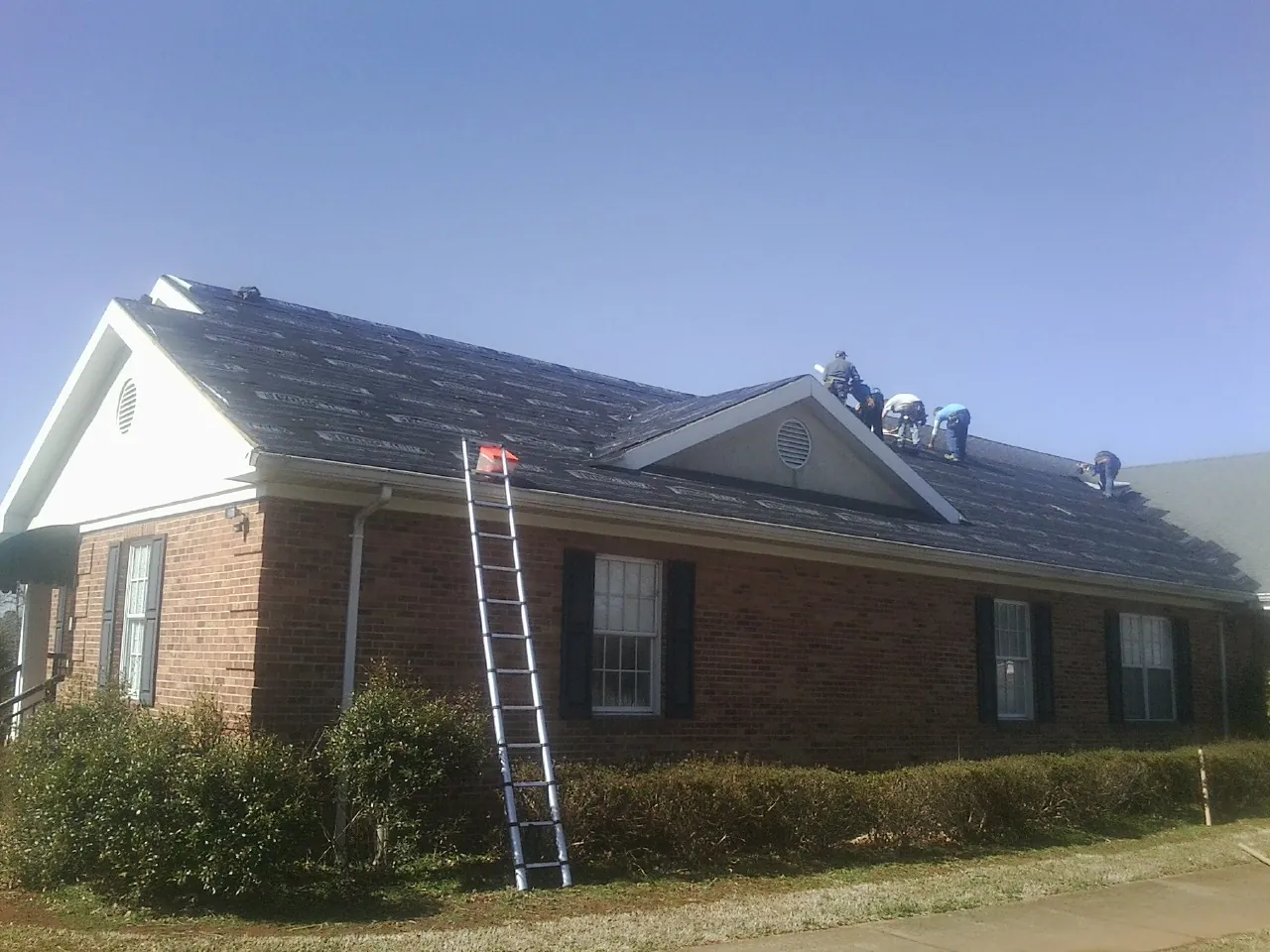 Crew tearing shingles off a brick ranch roof with a ladder set — Metal Roof Repair work by our crew in Epsom