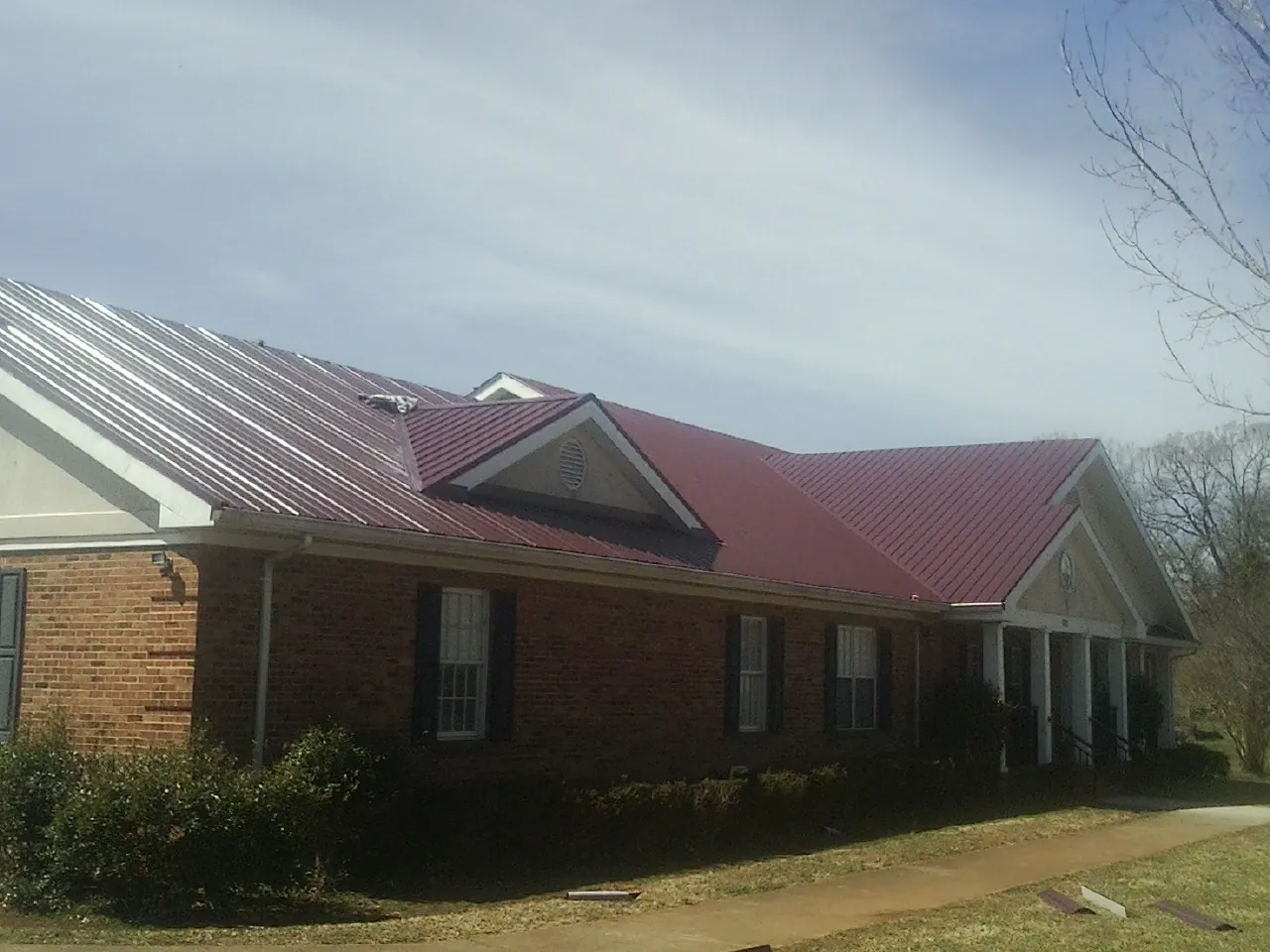 Red metal roof with gabled entries on a long brick building, from a Hail Damage Roof Repair job in Epsom