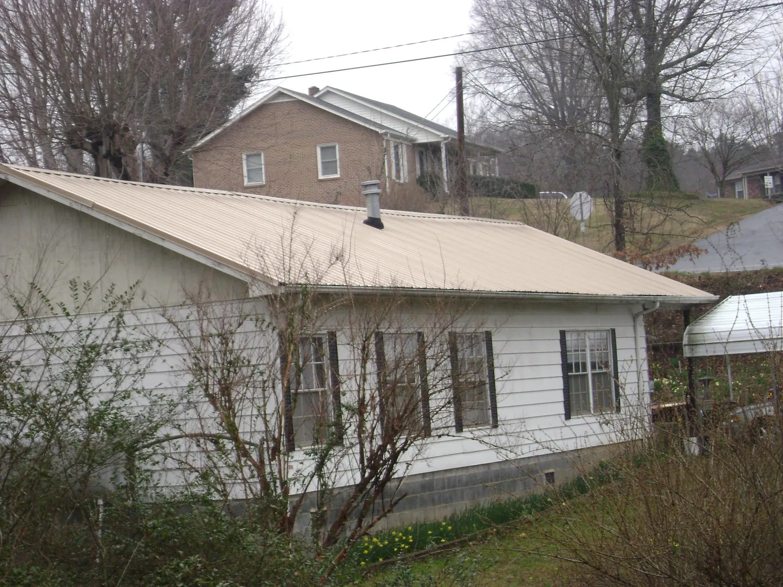 Tan metal roof on a white sided house set into a hillside — Commercial Roofing by Roofing Brothers in Epsom